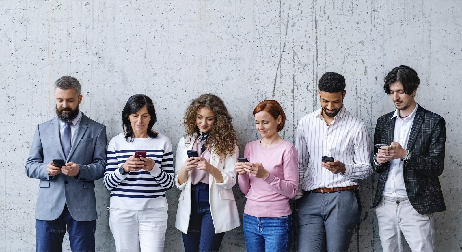 Gruppe von Menschen aus verschiedenen Berufen mit ihren Smartphones an einer Wand